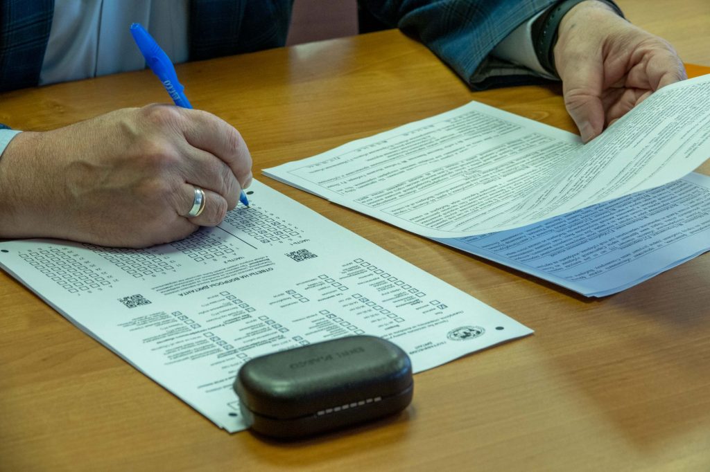 Gros plan sur les mains d'un homme remplissant un document officiel au stylo sur une table en bois