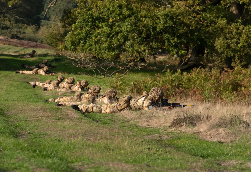 Un groupe de soldats en treillis rampe à travers un champ herbeux lors d'un exercice militaire