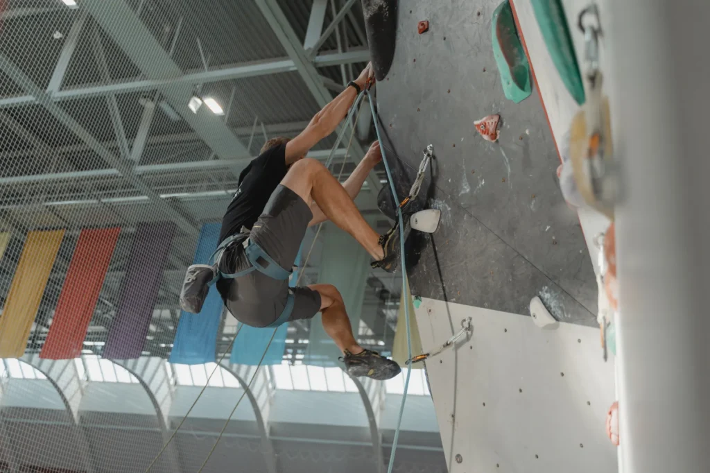 Un homme grimpe un mur d'escalade intérieur aux prises colorées, concentration et effort visibles