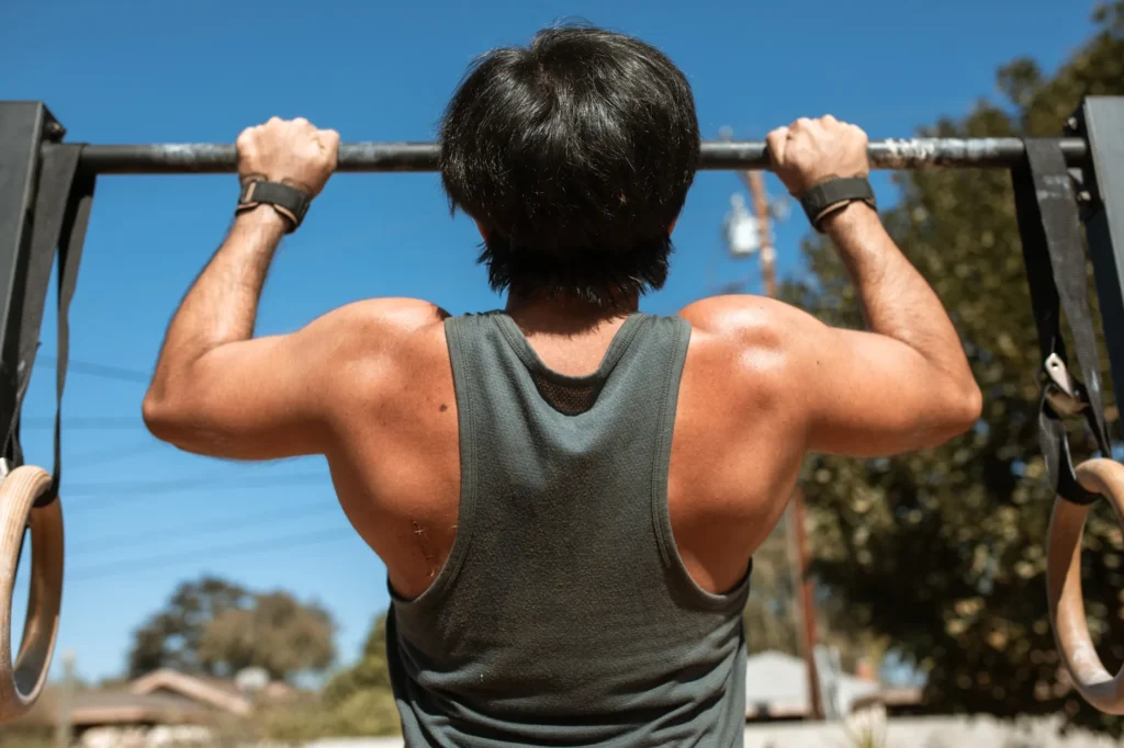 Homme faisant des tractions à une barre en extérieur, lumière naturelle, posture concentrée.